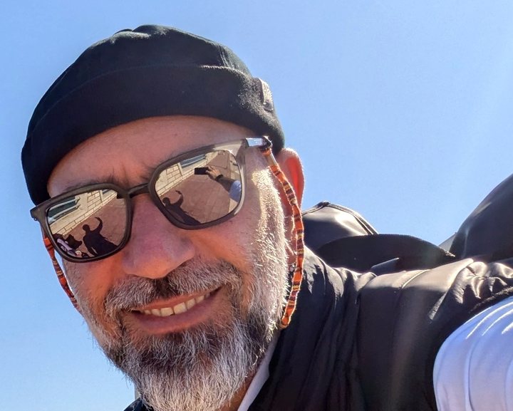 Rocco Pulizzi all’aperto, sorridente, con occhiali da sole e zaino.